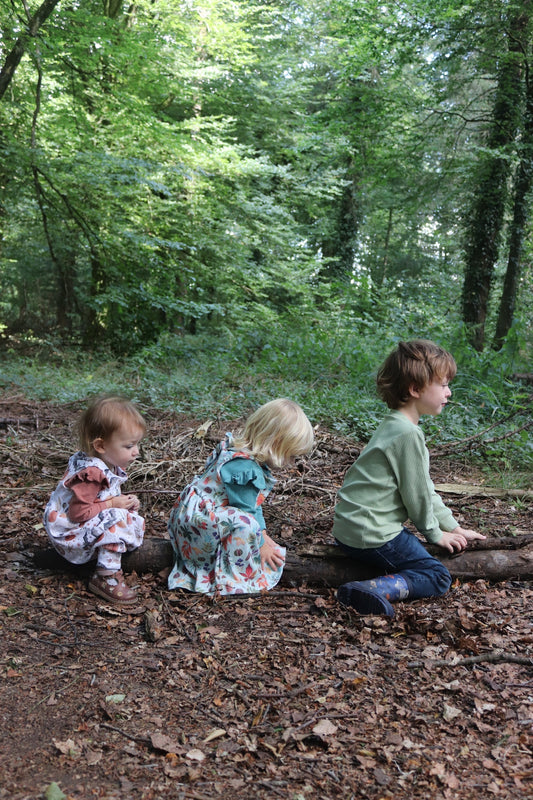 Three children playing outside in the woods in durable handmade organic clothing