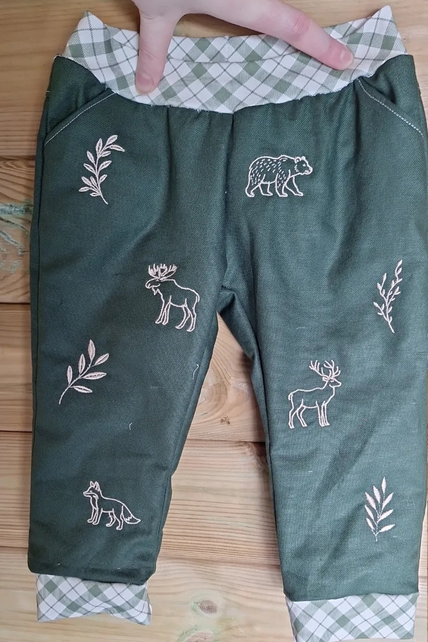 Forest green trousers with multiple embroidery designs spread across the legs, including bear, moose, fox, deer and foliage.